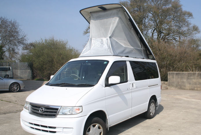 A white Mazda Bongo with its pop-top roof extended, ready for repair or MOT.